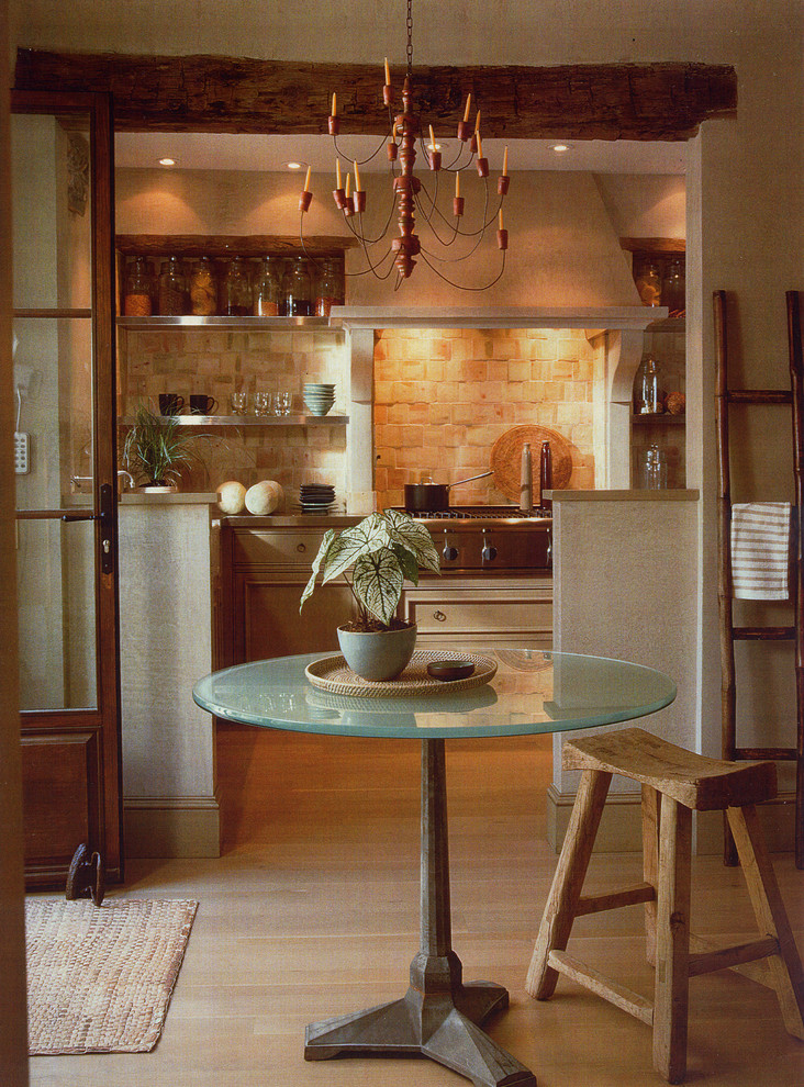 На фото: кухня в средиземноморском стиле с бежевым фартуком, фартуком из каменной плитки, техникой из нержавеющей стали и светлым паркетным полом