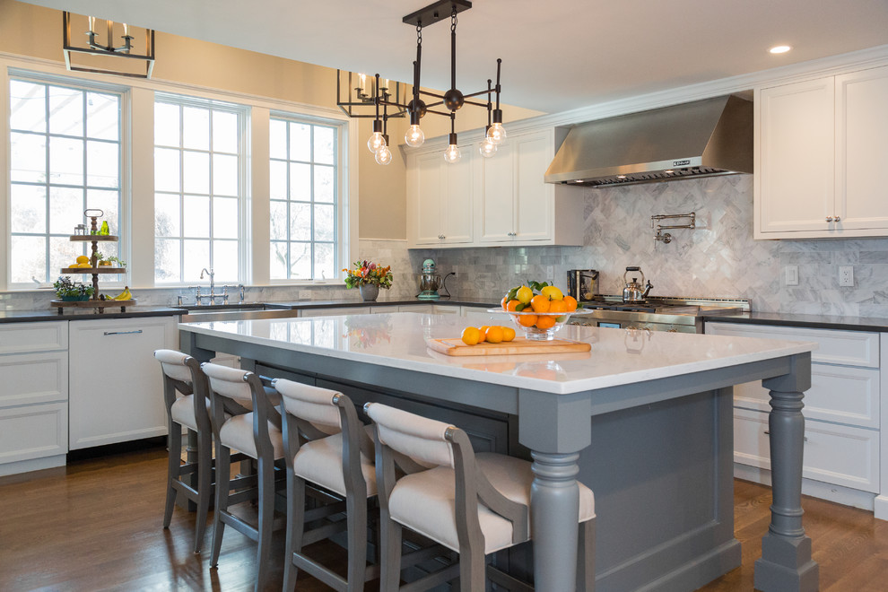 Inspiration for a timeless l-shaped medium tone wood floor kitchen remodel in Boston with a farmhouse sink, recessed-panel cabinets, white cabinets, multicolored backsplash, stainless steel appliances, an island and black countertops