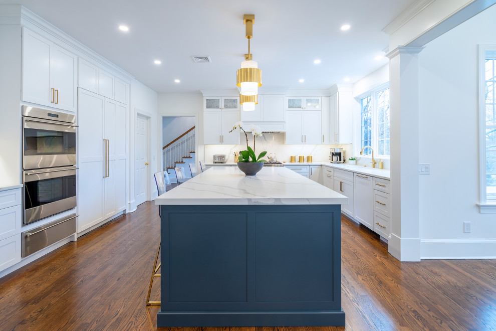 This is an example of a large classic kitchen in Philadelphia with a submerged sink, shaker cabinets, white cabinets, engineered stone countertops, white splashback, engineered quartz splashback, stainless steel appliances, dark hardwood flooring, an island, brown floors and white worktops.