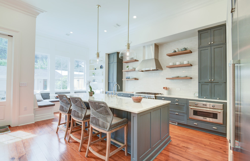 Photo of a medium sized traditional l-shaped kitchen in New Orleans with a submerged sink, recessed-panel cabinets, blue cabinets, white splashback, stainless steel appliances, medium hardwood flooring, an island and white worktops.