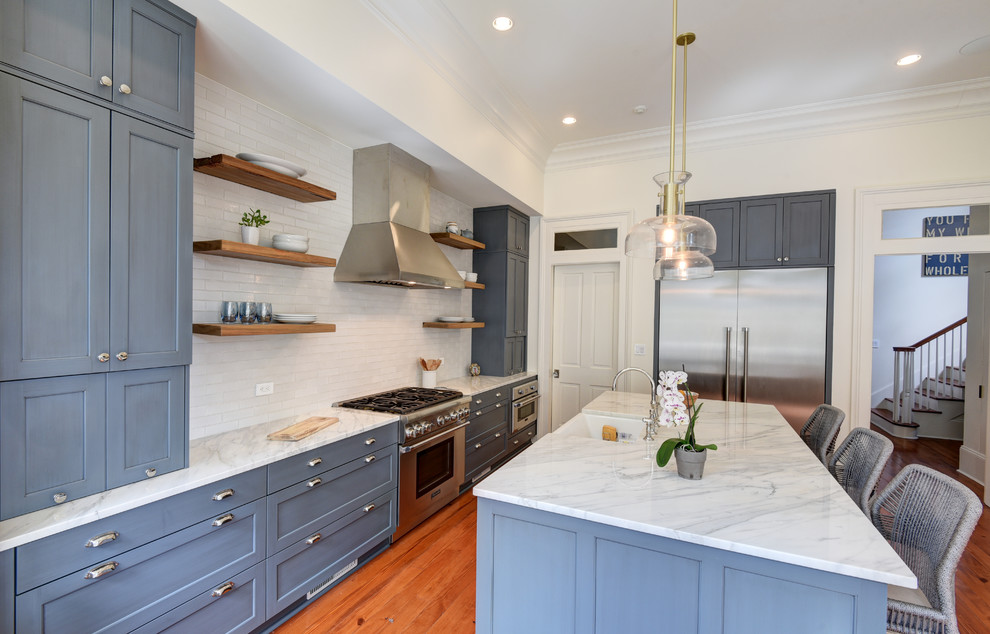 Klassisk inredning av ett mellanstort vit vitt l-kök, med en undermonterad diskho, luckor med infälld panel, blå skåp, vitt stänkskydd, rostfria vitvaror, mellanmörkt trägolv och en köksö