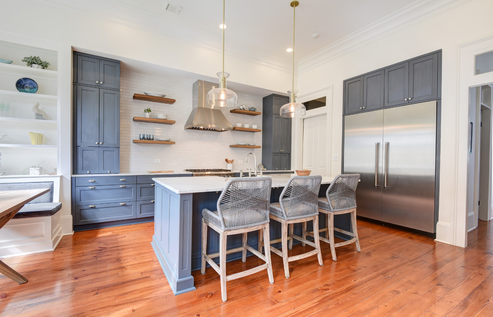 Mid-sized transitional l-shaped medium tone wood floor and brown floor kitchen photo in New Orleans with recessed-panel cabinets, blue cabinets, white backsplash, stainless steel appliances, an island and white countertops
