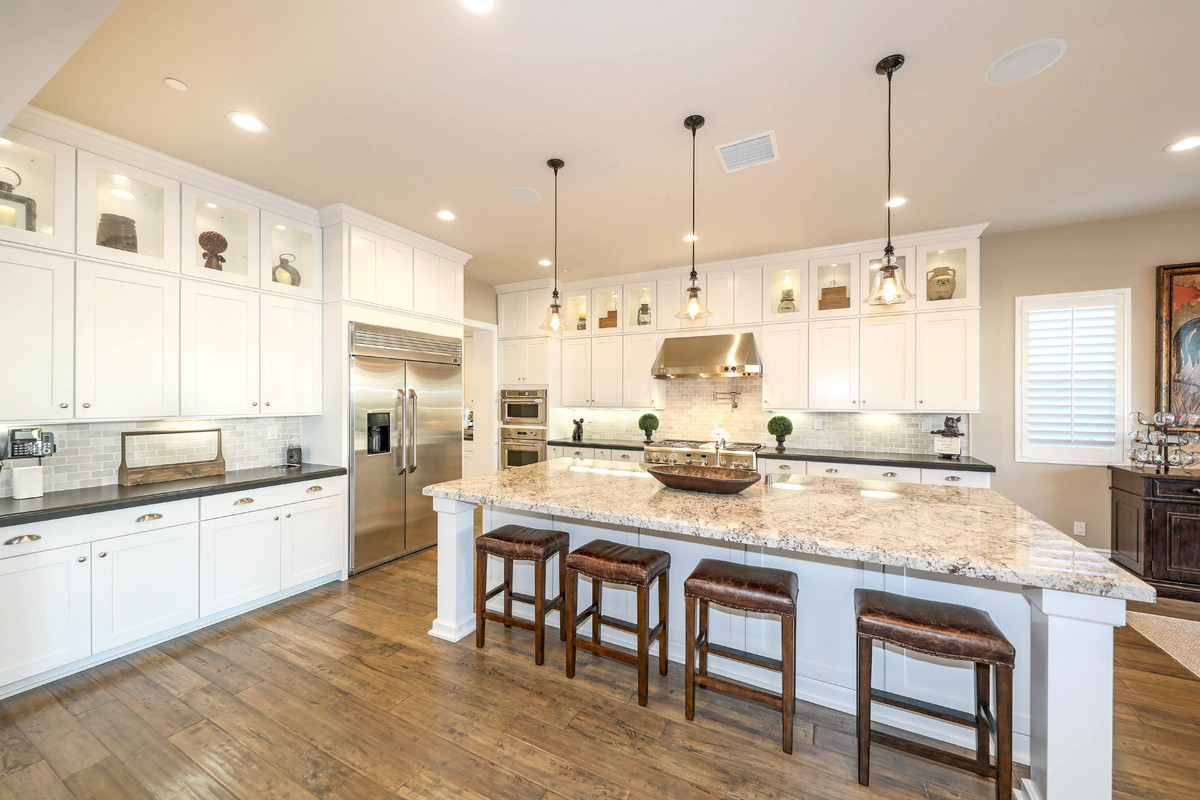 Inspiration for a large traditional l-shaped open plan kitchen in Orange County with shaker cabinets, white cabinets, stainless steel appliances, medium hardwood flooring, brown floors, a belfast sink, engineered stone countertops, beige splashback, metro tiled splashback and an island.