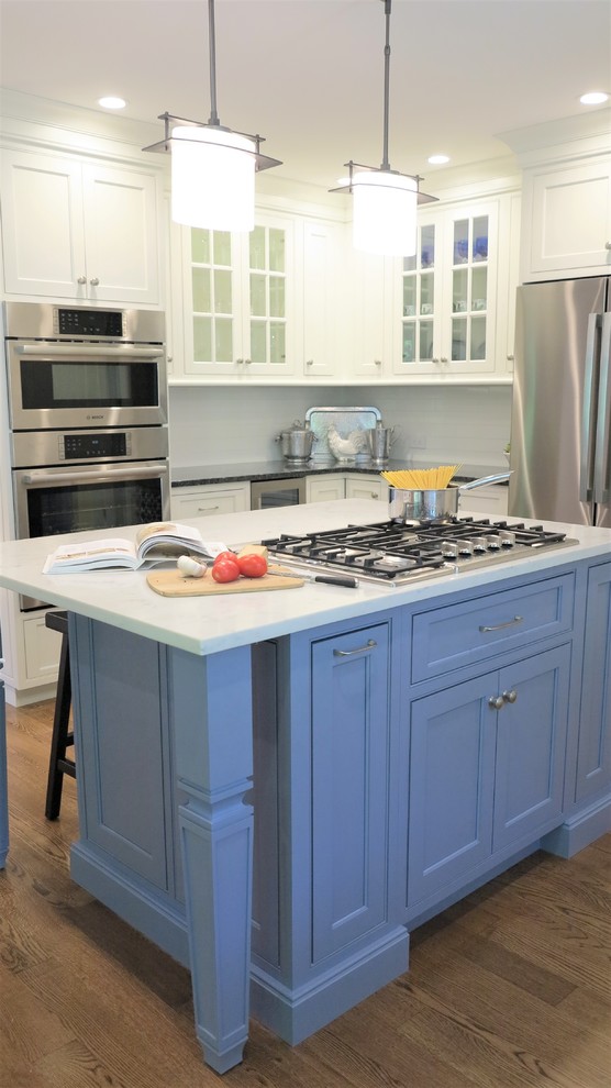 Inspiration för ett mellanstort vintage vit vitt kök, med luckor med profilerade fronter, blå skåp, rostfria vitvaror, mellanmörkt trägolv, en köksö, en undermonterad diskho, bänkskiva i kvarts, vitt stänkskydd och stänkskydd i tunnelbanekakel