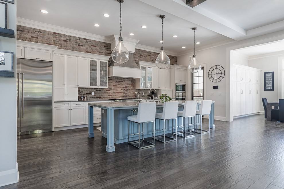 Open concept kitchen - large transitional l-shaped dark wood floor and brown floor open concept kitchen idea in Tampa with a farmhouse sink, shaker cabinets, white cabinets, quartzite countertops, red backsplash, brick backsplash, stainless steel appliances and an island