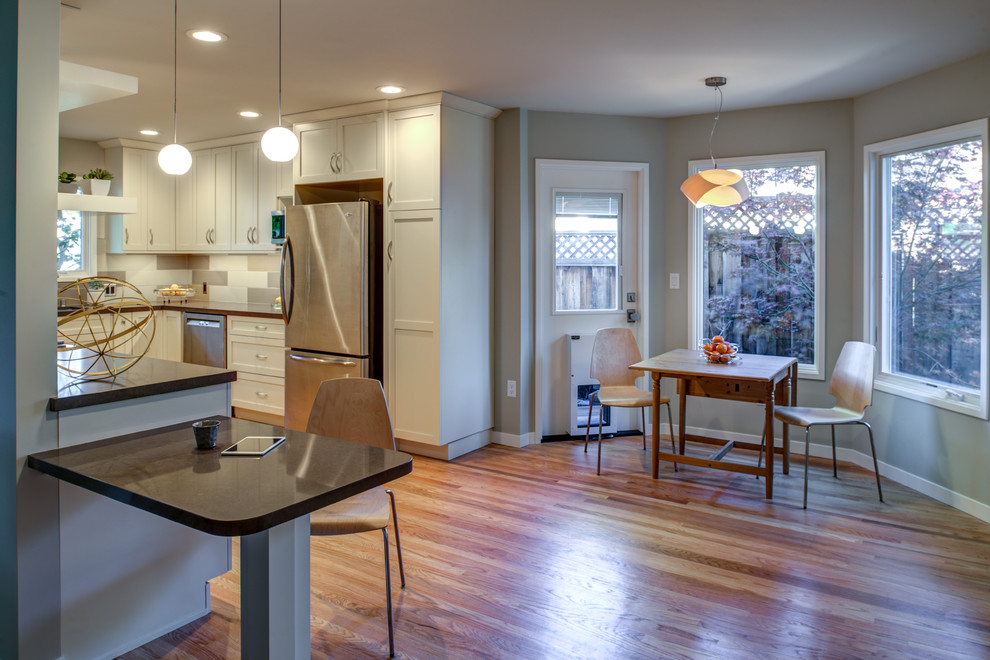 This is an example of a small classic u-shaped kitchen/diner in San Francisco with a submerged sink, shaker cabinets, white cabinets, engineered stone countertops, multi-coloured splashback, porcelain splashback, stainless steel appliances, light hardwood flooring and a breakfast bar.