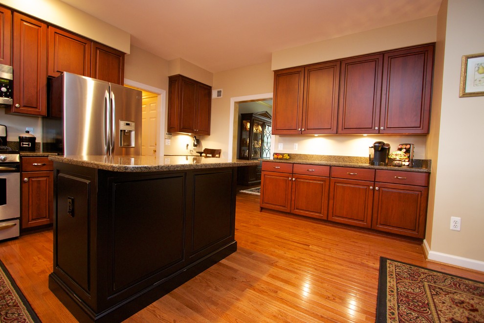 Klassische Küche mit profilierten Schrankfronten, hellbraunen Holzschränken, Granit-Arbeitsplatte, Küchengeräten aus Edelstahl, braunem Holzboden und Kücheninsel in Baltimore