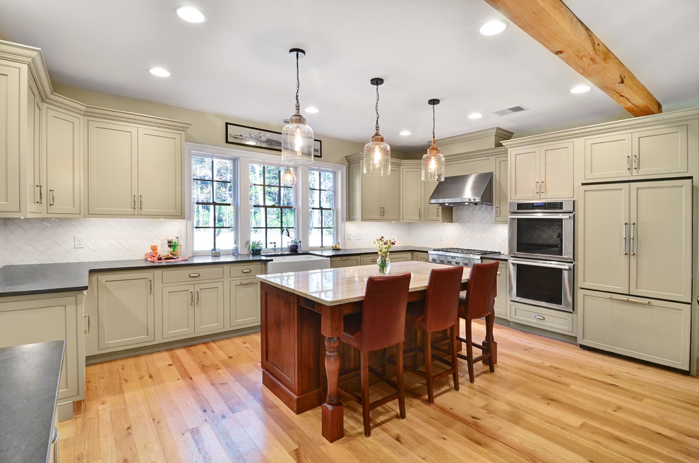 Large cottage u-shaped brown floor and light wood floor kitchen photo in Baltimore with a farmhouse sink, shaker cabinets, beige cabinets, white backsplash, an island, soapstone countertops, glass tile backsplash and paneled appliances