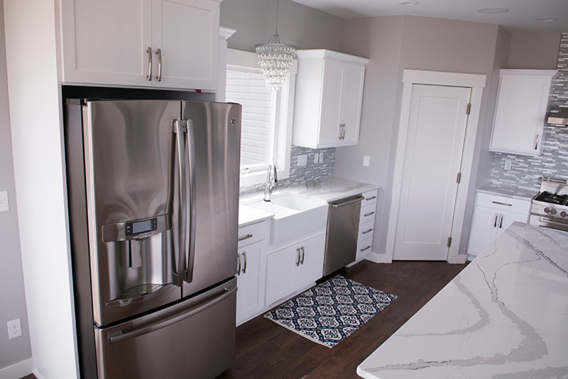 Photo of a large contemporary l-shaped open plan kitchen in Other with a belfast sink, white cabinets, stainless steel appliances, dark hardwood flooring, an island, brown floors, shaker cabinets, engineered stone countertops, multi-coloured splashback, matchstick tiled splashback and white worktops.