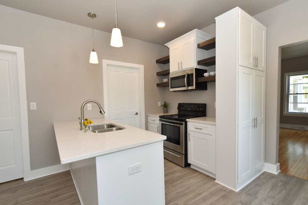 Small classic galley enclosed kitchen in Milwaukee with a submerged sink, shaker cabinets, white cabinets, quartz worktops, stainless steel appliances, vinyl flooring, a breakfast bar, brown floors and white worktops.