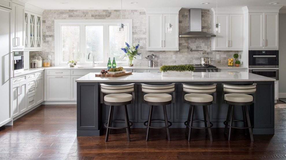 Inspiration for a large transitional l-shaped dark wood floor and brown floor kitchen remodel in Other with white cabinets, quartz countertops, gray backsplash, stainless steel appliances, an island, an undermount sink, shaker cabinets and stone tile backsplash