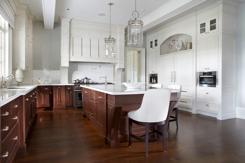 This is an example of an expansive traditional u-shaped kitchen/diner in Toronto with a submerged sink, recessed-panel cabinets, medium wood cabinets, composite countertops, white splashback, medium hardwood flooring, an island, stone slab splashback and integrated appliances.