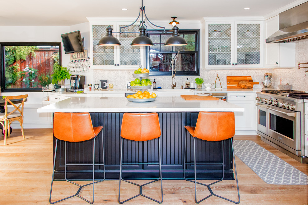 Example of a large transitional l-shaped medium tone wood floor and brown floor eat-in kitchen design in Los Angeles with a farmhouse sink, shaker cabinets, white cabinets, quartz countertops, white backsplash, porcelain backsplash, stainless steel appliances, an island and white countertops