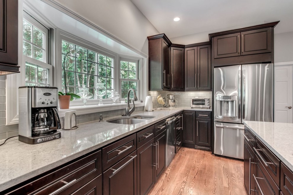 Inspiration for a large transitional galley light wood floor and brown floor eat-in kitchen remodel in Raleigh with an undermount sink, raised-panel cabinets, dark wood cabinets, quartz countertops, gray backsplash, glass tile backsplash, stainless steel appliances, an island and gray countertops