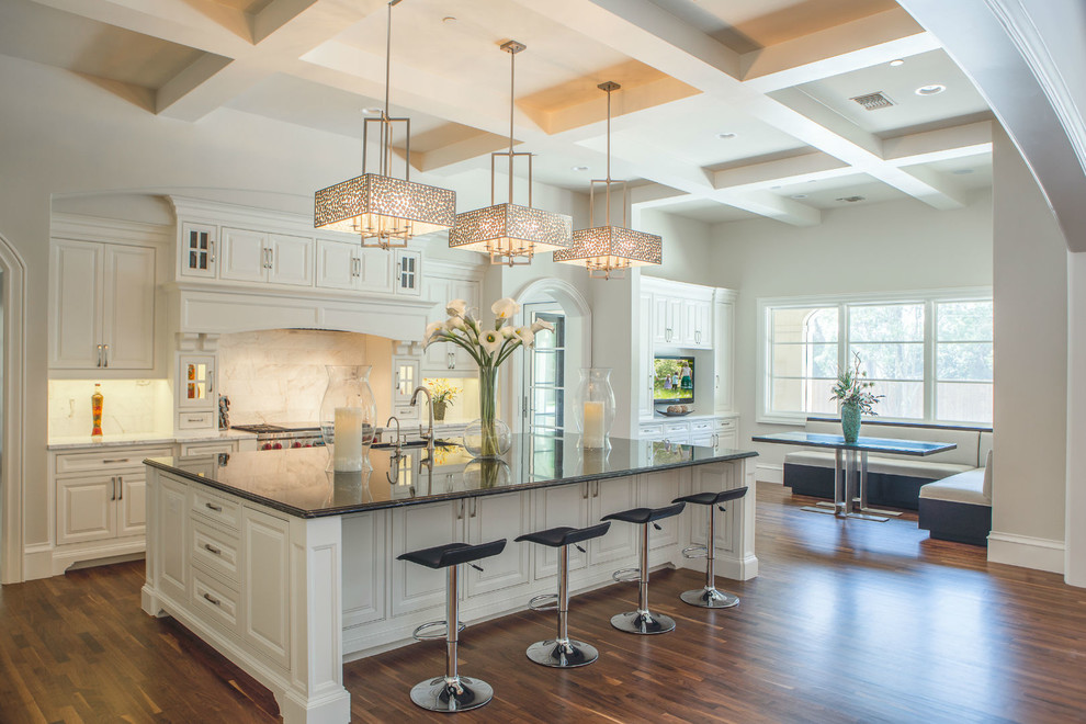 This is an example of an expansive traditional kitchen/diner in Dallas with a submerged sink, raised-panel cabinets, white cabinets, marble worktops, white splashback, stainless steel appliances, medium hardwood flooring and an island.