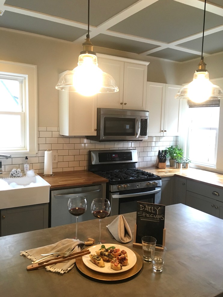 Inspiration for a large transitional l-shaped ceramic tile enclosed kitchen remodel in Cleveland with a farmhouse sink, shaker cabinets, white cabinets, concrete countertops, subway tile backsplash, stainless steel appliances and an island