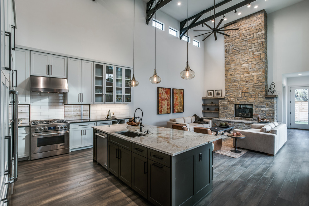 Example of a transitional l-shaped dark wood floor and brown floor open concept kitchen design in Dallas with an undermount sink, shaker cabinets, gray cabinets, granite countertops, white backsplash, porcelain backsplash, stainless steel appliances and an island