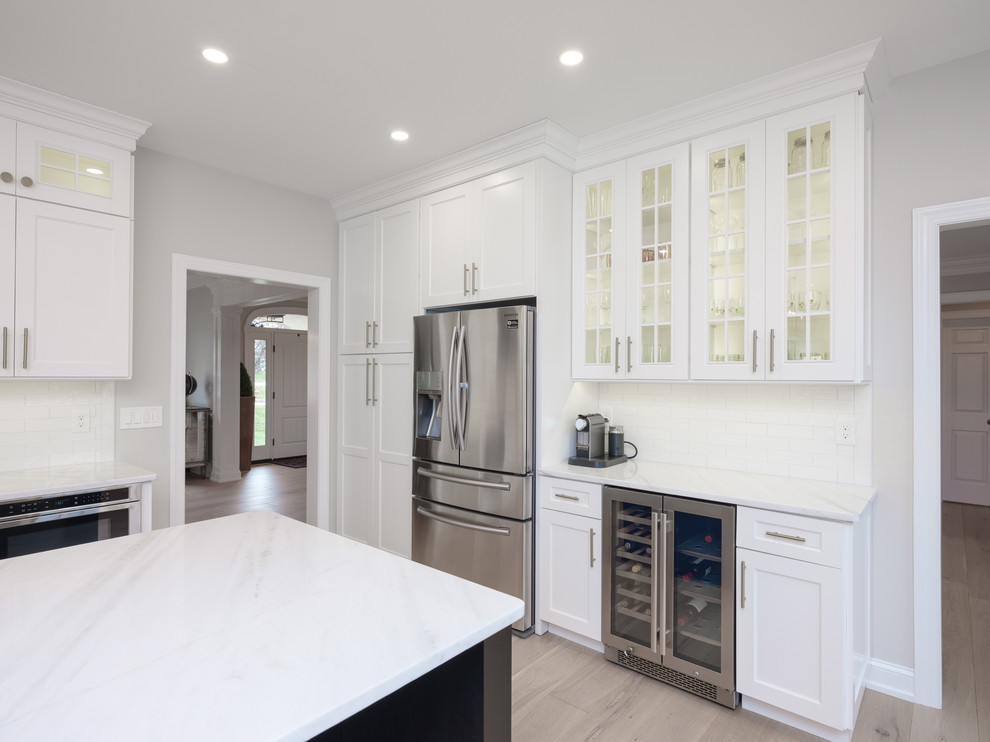 Inspiration for a large transitional light wood floor kitchen remodel in Philadelphia with an undermount sink, shaker cabinets, white cabinets, quartz countertops, white backsplash, porcelain backsplash, stainless steel appliances, an island and white countertops
