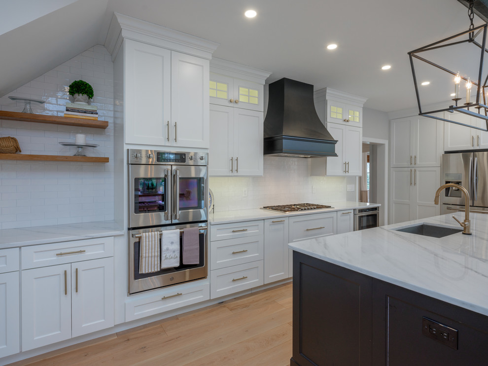 Example of a large transitional light wood floor kitchen design in Philadelphia with an undermount sink, shaker cabinets, white cabinets, quartz countertops, white backsplash, porcelain backsplash, stainless steel appliances, an island and white countertops