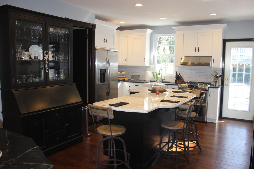 Example of a country medium tone wood floor kitchen design in Philadelphia with a farmhouse sink, shaker cabinets, white cabinets, soapstone countertops, white backsplash, subway tile backsplash, stainless steel appliances and an island