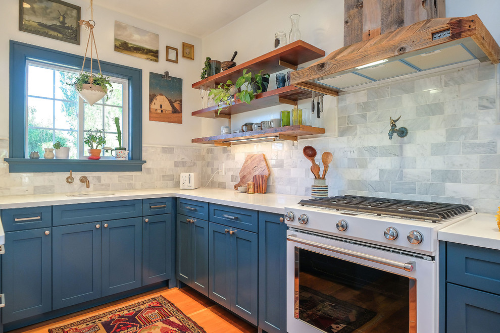 Modelo de cocinas en U tradicional renovado con armarios estilo shaker, puertas de armario azules, encimera de cuarcita, salpicadero de azulejos de porcelana, suelo de madera clara y península