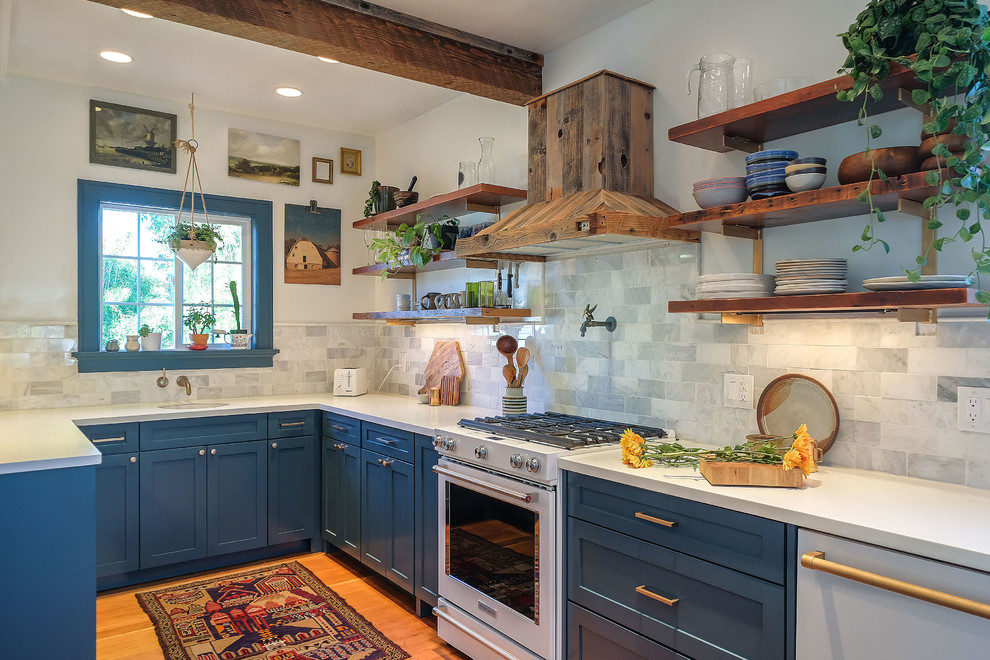 Inspiration pour une cuisine traditionnelle en U avec un placard à porte shaker, des portes de placard bleues, un plan de travail en quartz, une crédence en carreau de porcelaine, parquet clair et une péninsule.