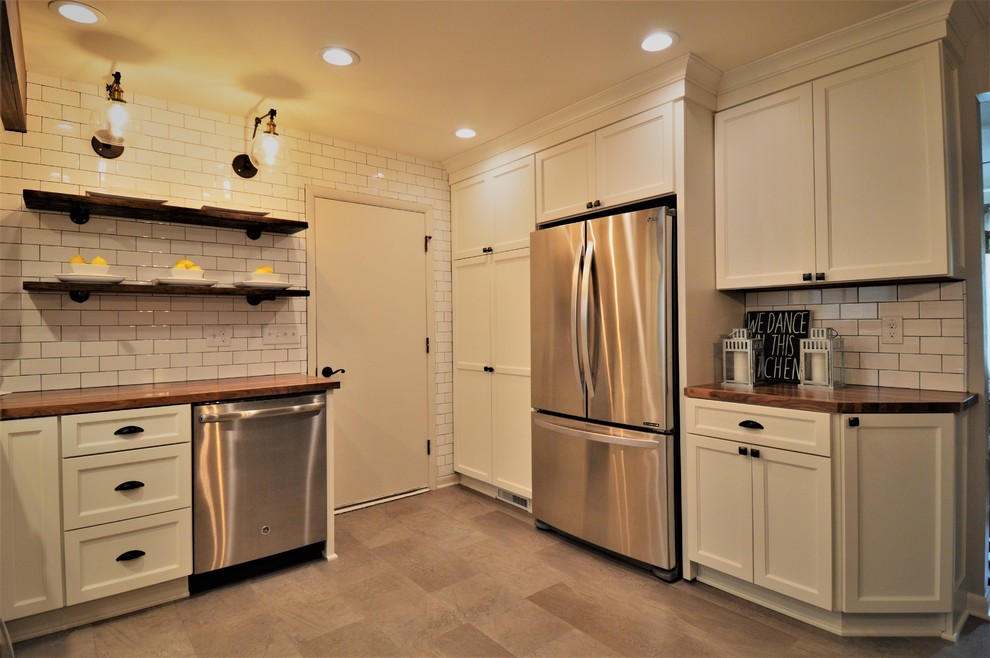 Example of a mid-sized country l-shaped vinyl floor and gray floor enclosed kitchen design in Milwaukee with a drop-in sink, shaker cabinets, white cabinets, wood countertops, white backsplash, ceramic backsplash and stainless steel appliances