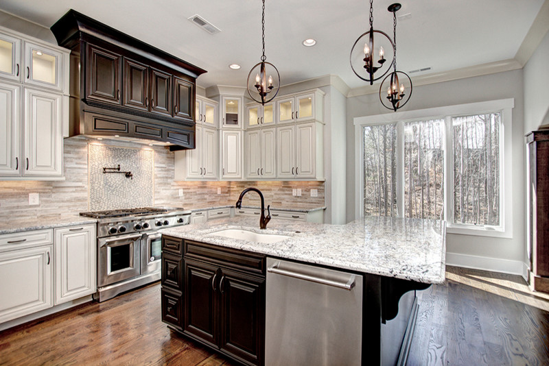This is an example of a large traditional u-shaped open plan kitchen in Charlotte with raised-panel cabinets, white cabinets, stainless steel appliances, medium hardwood flooring and an island.