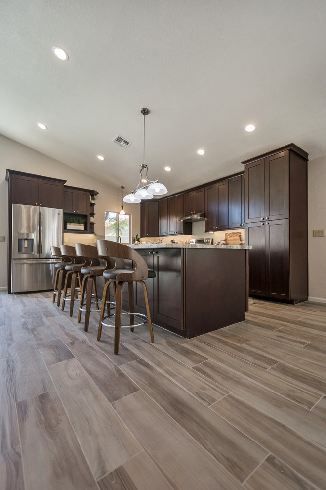 Mid-sized transitional l-shaped porcelain tile and brown floor open concept kitchen photo in Phoenix with an undermount sink, shaker cabinets, brown cabinets, granite countertops, gray backsplash, glass tile backsplash, stainless steel appliances, an island and multicolored countertops