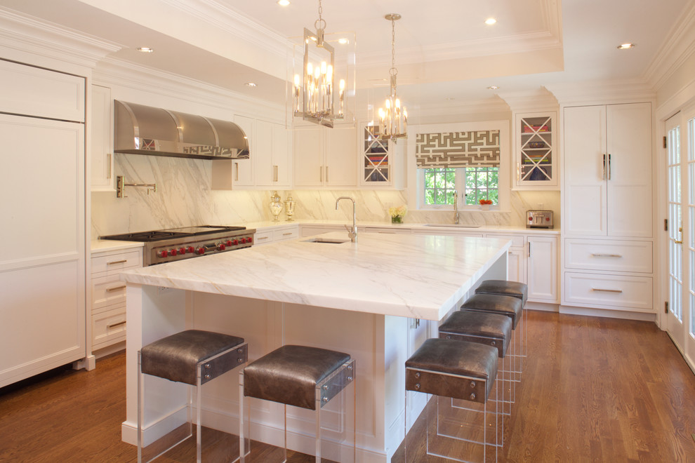 Photo of a large classic u-shaped kitchen/diner in New York with white cabinets, marble worktops, stone slab splashback, integrated appliances, medium hardwood flooring, an island, a submerged sink and recessed-panel cabinets.