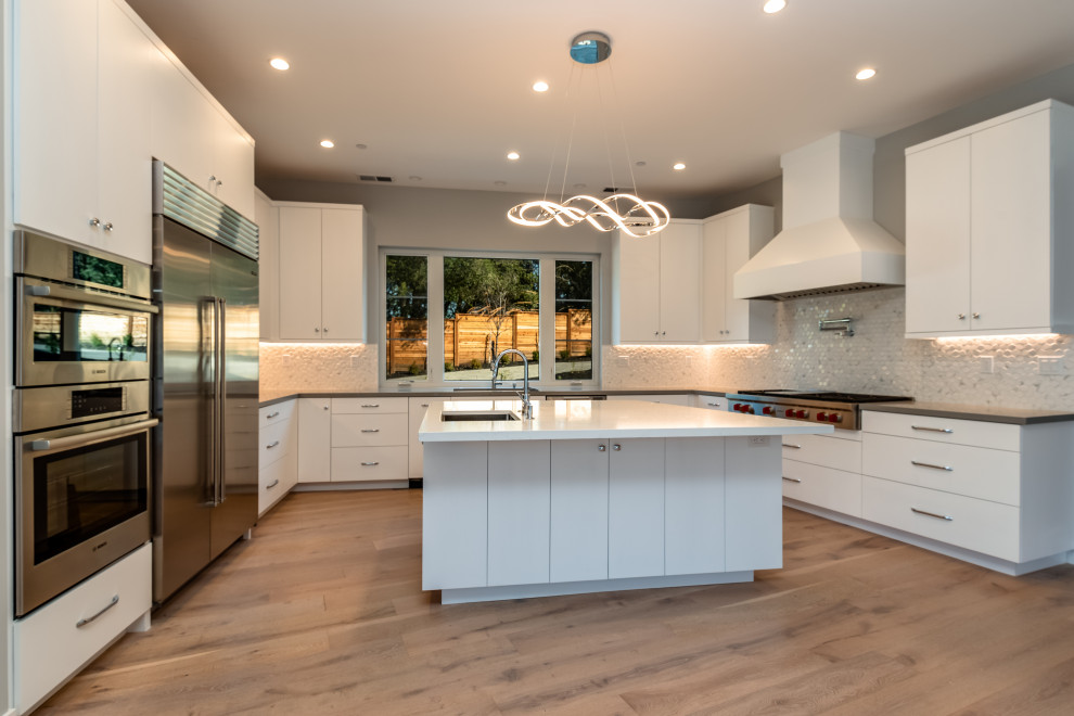 Large transitional u-shaped light wood floor and white floor eat-in kitchen photo in San Francisco with an undermount sink, flat-panel cabinets, white cabinets, quartz countertops, white backsplash, porcelain backsplash, stainless steel appliances, an island and white countertops