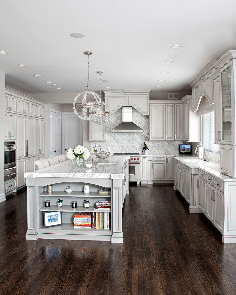 This is an example of a large traditional u-shaped open plan kitchen in Newark with a submerged sink, raised-panel cabinets, grey cabinets, marble worktops, white splashback, stone slab splashback, stainless steel appliances, dark hardwood flooring and an island.