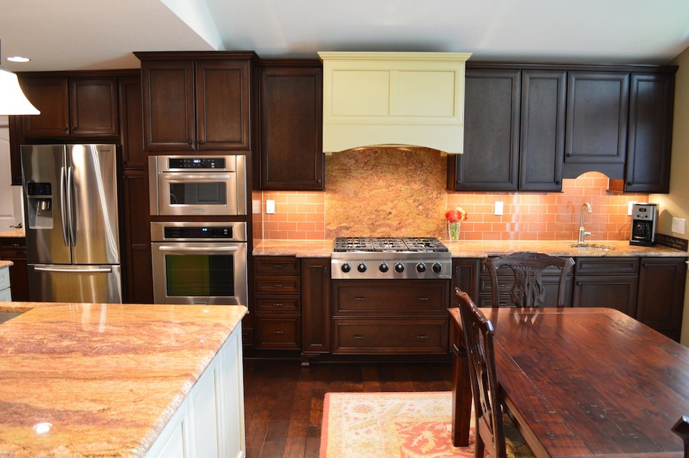 Klassisk inredning av ett mellanstort kök, med en nedsänkt diskho, släta luckor, skåp i mörkt trä, granitbänkskiva, orange stänkskydd, stänkskydd i glaskakel, rostfria vitvaror och mörkt trägolv