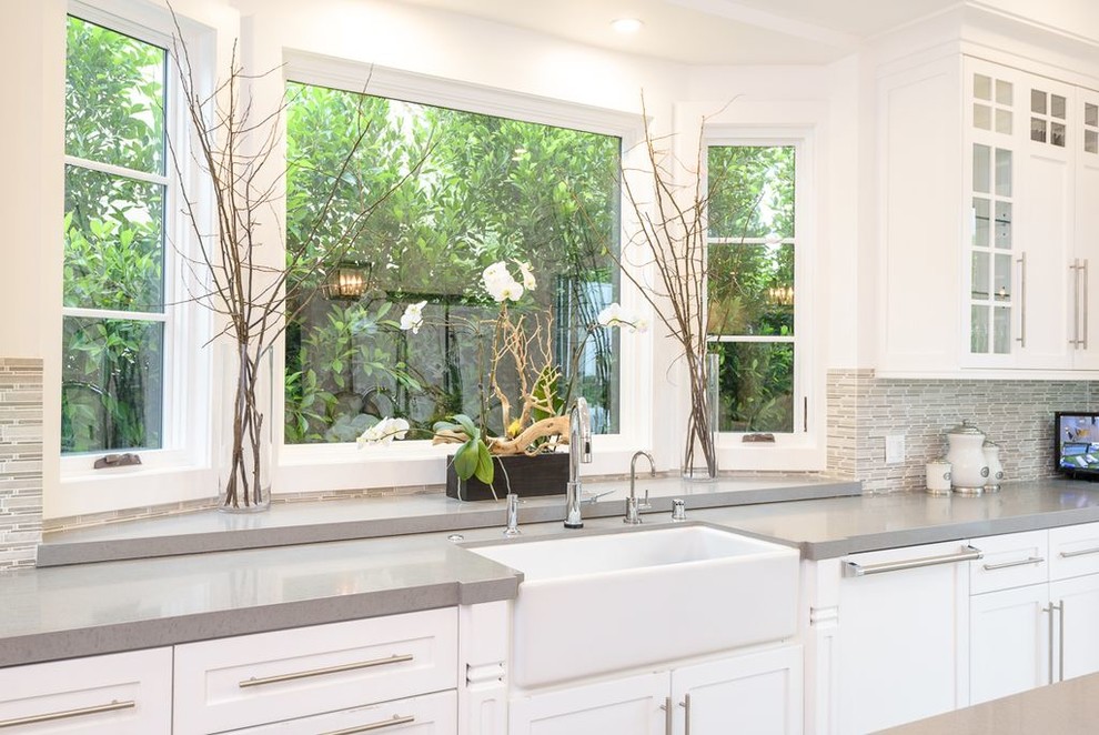 Inspiration for a large transitional l-shaped light wood floor and gray floor eat-in kitchen remodel in Los Angeles with a farmhouse sink, shaker cabinets, white cabinets, green backsplash, glass tile backsplash, stainless steel appliances, an island, gray countertops and granite countertops