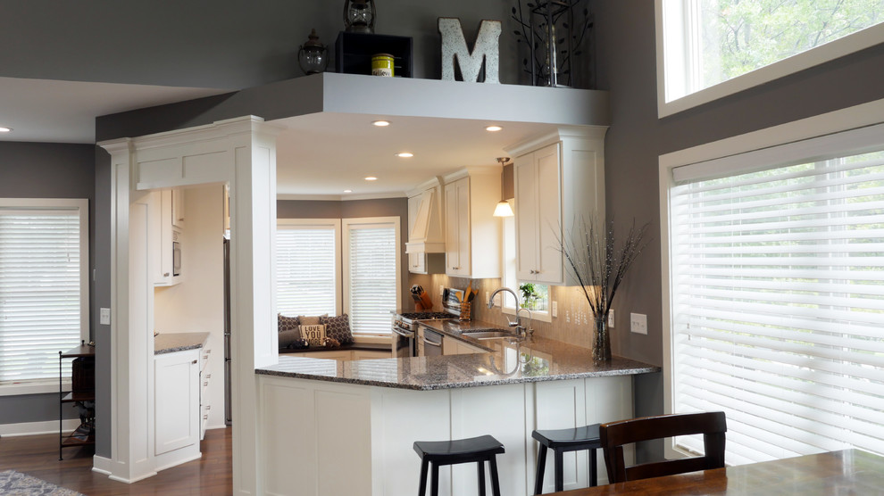 Inredning av ett klassiskt litet grå grått kök, med en undermonterad diskho, släta luckor, vita skåp, granitbänkskiva, grått stänkskydd, stänkskydd i cementkakel, rostfria vitvaror, mellanmörkt trägolv, en halv köksö och brunt golv