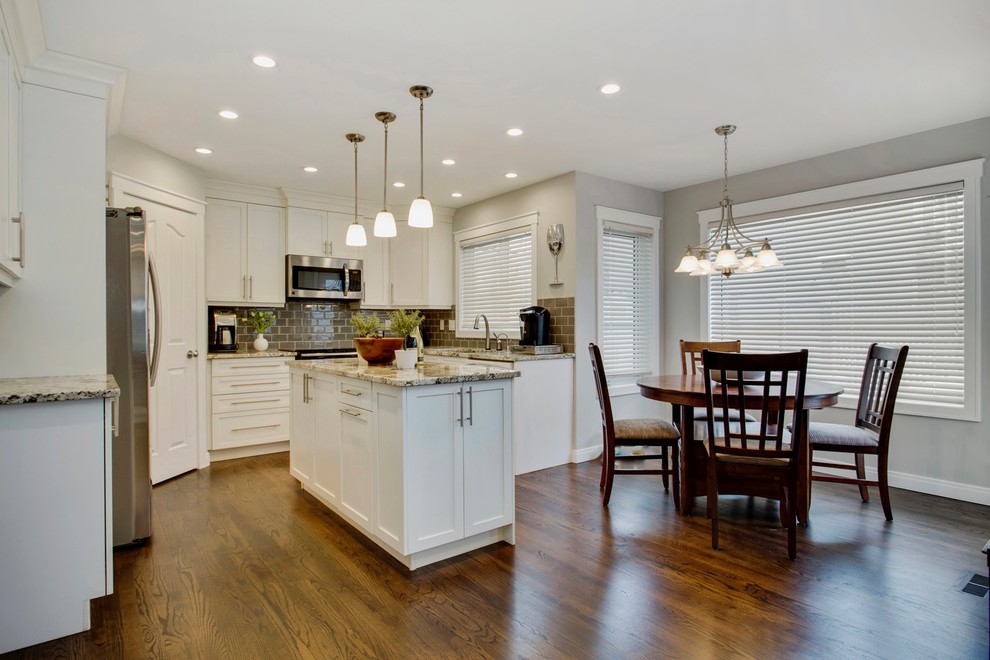 Example of a small transitional u-shaped dark wood floor enclosed kitchen design in Other with an undermount sink, shaker cabinets, white cabinets, granite countertops, gray backsplash, porcelain backsplash, stainless steel appliances and an island