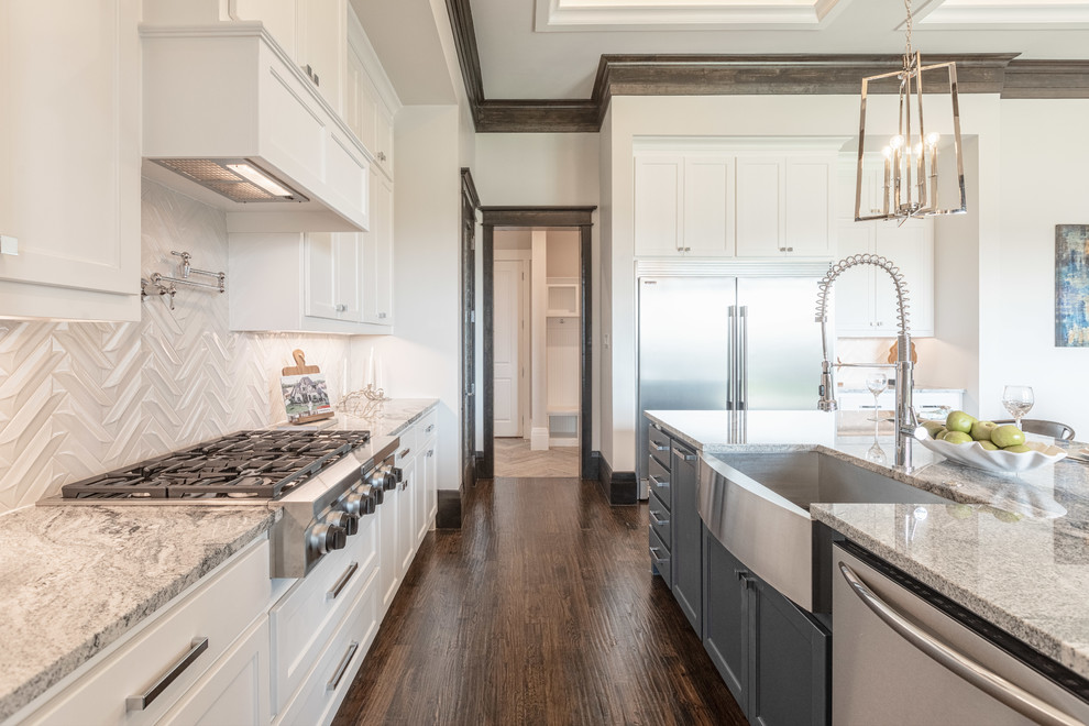 Photo of a large traditional l-shaped open plan kitchen in Dallas with a belfast sink, raised-panel cabinets, white cabinets, granite worktops, white splashback, porcelain splashback, stainless steel appliances, medium hardwood flooring, an island, brown floors and grey worktops.