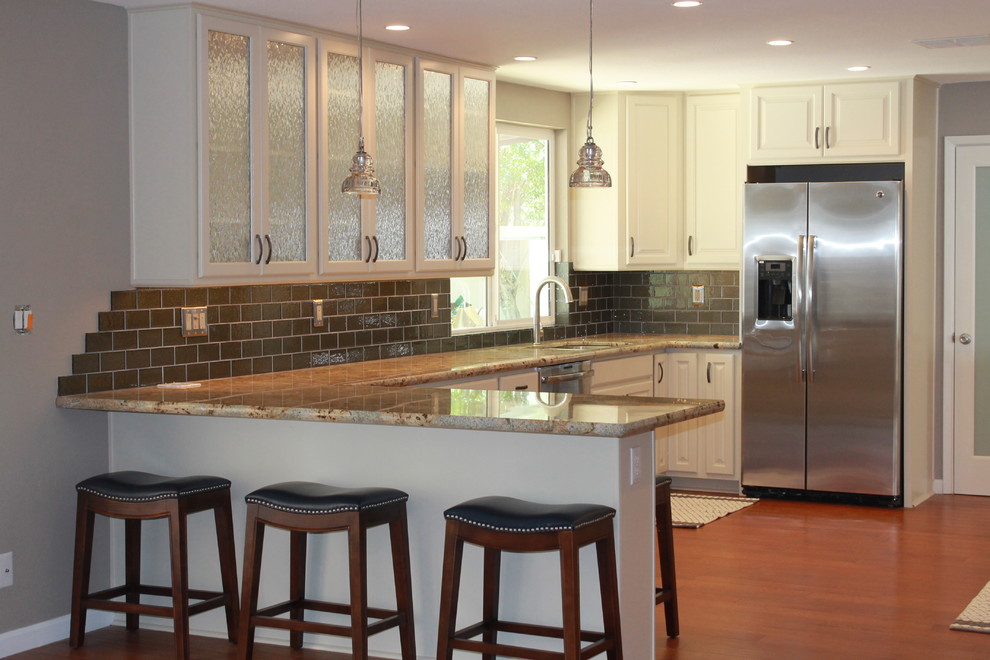 Eat-in kitchen - mid-sized transitional u-shaped dark wood floor and brown floor eat-in kitchen idea in Phoenix with an undermount sink, raised-panel cabinets, white cabinets, granite countertops, green backsplash, glass tile backsplash, stainless steel appliances and a peninsula