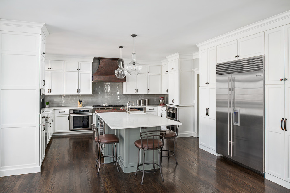 Example of a large transitional u-shaped dark wood floor and brown floor open concept kitchen design in Chicago with a farmhouse sink, flat-panel cabinets, white cabinets, quartz countertops, gray backsplash, glass tile backsplash, stainless steel appliances, an island and white countertops