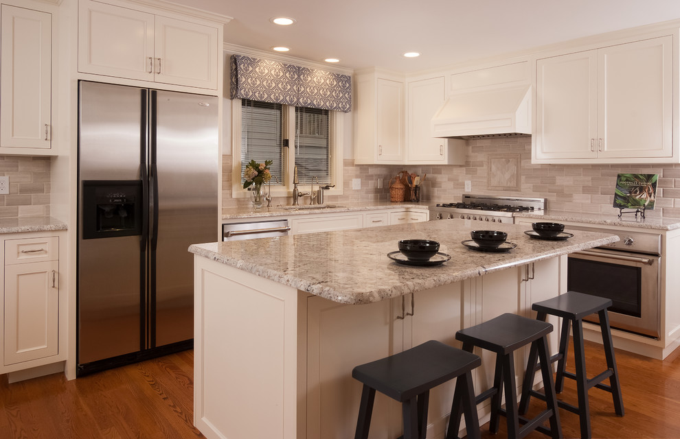 Example of a mid-sized transitional l-shaped medium tone wood floor and brown floor enclosed kitchen design in Other with an undermount sink, recessed-panel cabinets, white cabinets, quartz countertops, gray backsplash, stone tile backsplash, stainless steel appliances, an island and gray countertops