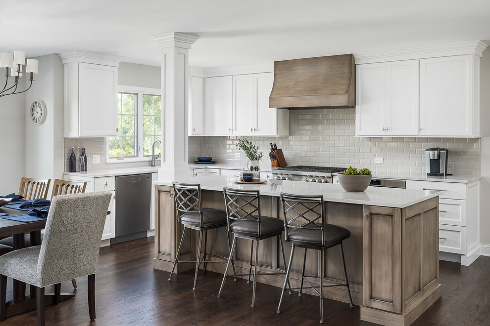 Design ideas for a large classic l-shaped kitchen/diner in Chicago with shaker cabinets, white cabinets, grey splashback, metro tiled splashback, stainless steel appliances, dark hardwood flooring, an island, brown floors, engineered stone countertops and white worktops.