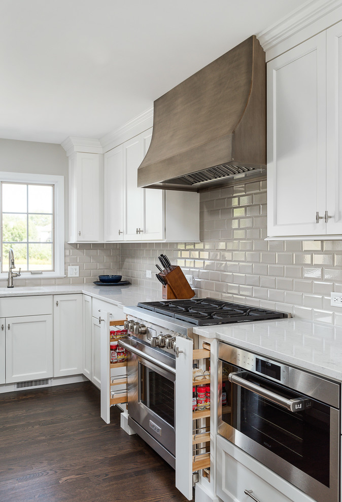 Large traditional l-shaped open plan kitchen in Chicago with flat-panel cabinets, white cabinets, engineered stone countertops, grey splashback, ceramic splashback, stainless steel appliances, dark hardwood flooring, an island, brown floors and white worktops.