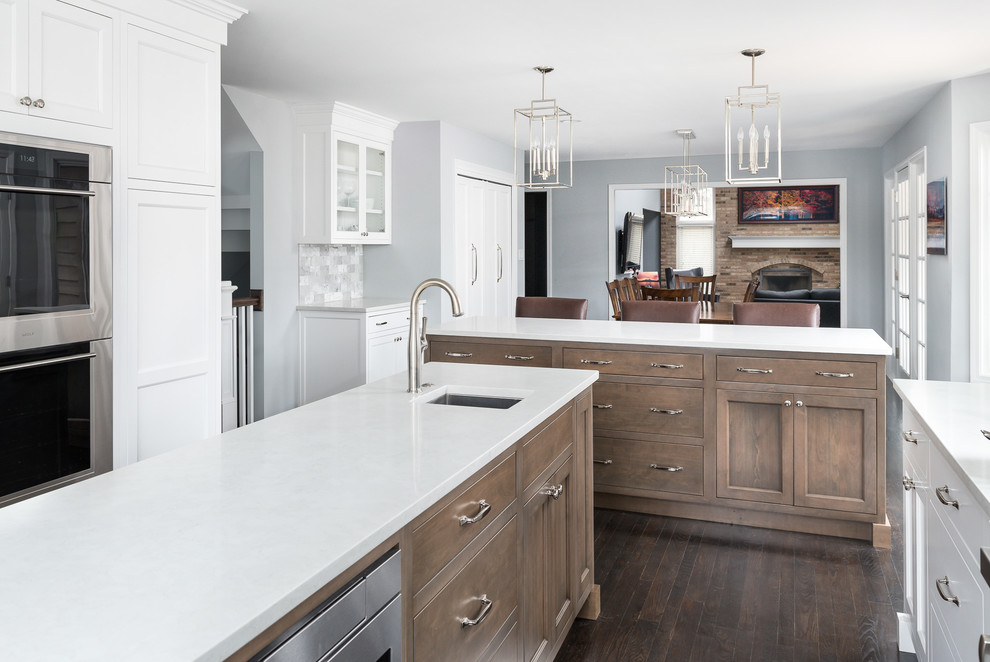 Example of a mid-sized transitional u-shaped dark wood floor and brown floor eat-in kitchen design in Chicago with an undermount sink, white cabinets, quartz countertops, marble backsplash, stainless steel appliances, white countertops, recessed-panel cabinets, gray backsplash and an island