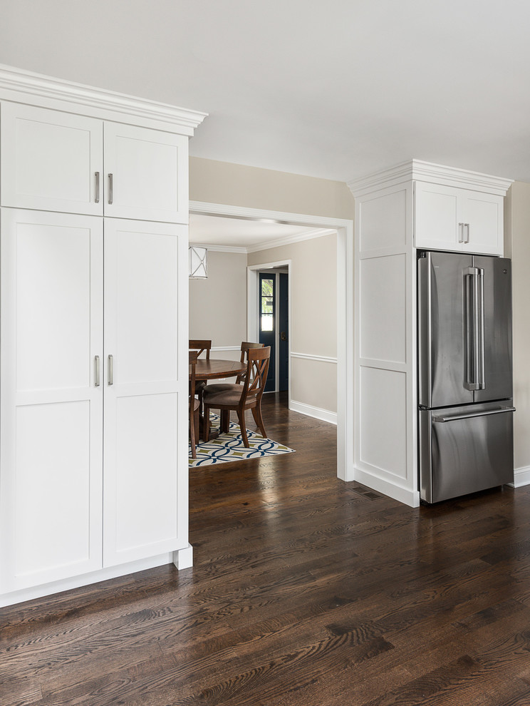 This is an example of a large classic l-shaped open plan kitchen in Chicago with white cabinets, engineered stone countertops, white splashback, brick splashback, stainless steel appliances, medium hardwood flooring, multiple islands, brown floors, white worktops, a submerged sink and shaker cabinets.