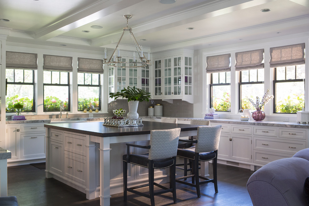 Cette image montre une cuisine américaine traditionnelle avec des portes de placard blanches, une crédence grise, un électroménager en acier inoxydable, parquet foncé et îlot.
