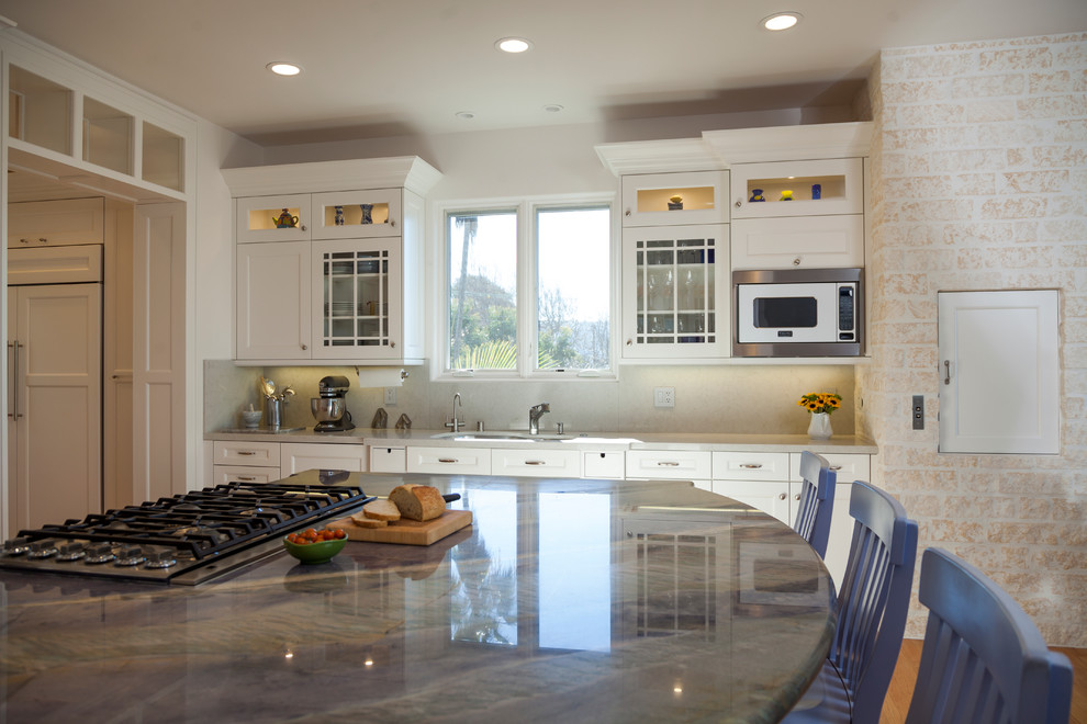 This is an example of a large traditional kitchen/diner in Los Angeles with a submerged sink, recessed-panel cabinets, white cabinets, quartz worktops, grey splashback, stone slab splashback, integrated appliances, light hardwood flooring and an island.
