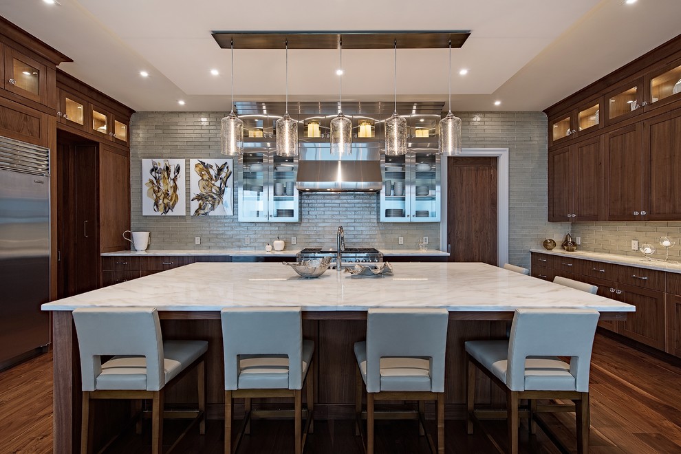 Example of a transitional u-shaped medium tone wood floor and brown floor kitchen design in Raleigh with an undermount sink, shaker cabinets, brown cabinets, gray backsplash, subway tile backsplash, stainless steel appliances, an island and white countertops