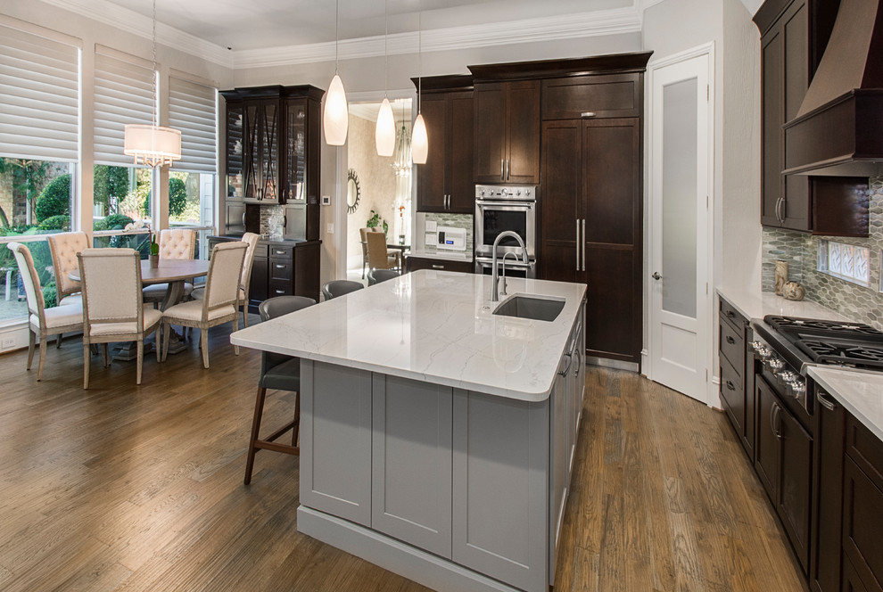 This is an example of a medium sized traditional l-shaped open plan kitchen in DC Metro with a submerged sink, recessed-panel cabinets, dark wood cabinets, granite worktops, beige splashback, ceramic splashback, stainless steel appliances, medium hardwood flooring, an island, brown floors and beige worktops.