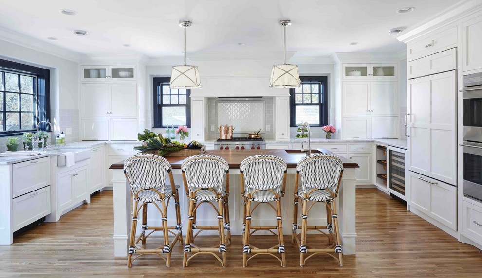 Inspiration for a transitional u-shaped medium tone wood floor and brown floor kitchen remodel in DC Metro with a farmhouse sink, shaker cabinets, white cabinets, marble countertops, white backsplash, paneled appliances, an island and gray countertops