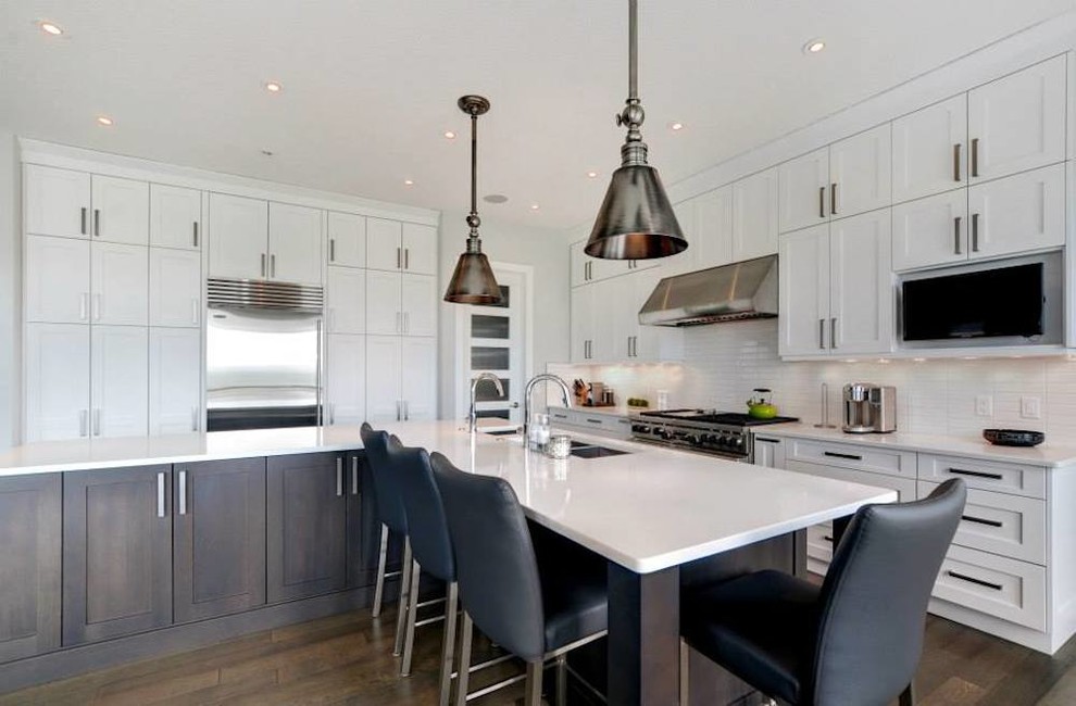 Inspiration for a transitional l-shaped dark wood floor enclosed kitchen remodel in Calgary with a triple-bowl sink, shaker cabinets, white cabinets, quartzite countertops, white backsplash, ceramic backsplash, stainless steel appliances and an island